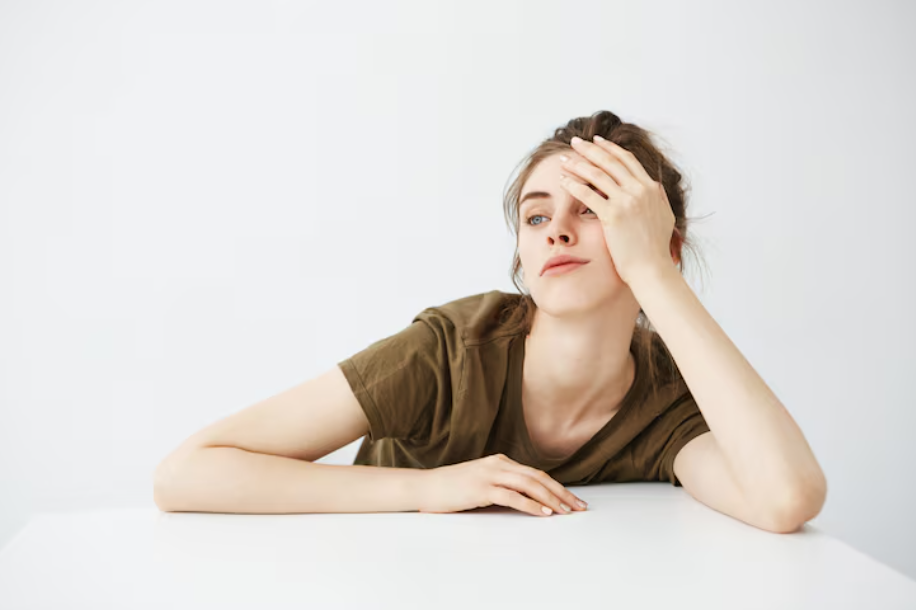 Tired young woman leaning on a desk with a blank stare, illustrating boredom.