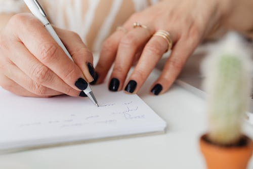 Close-up of a hand writing notes with a pen on white paper.