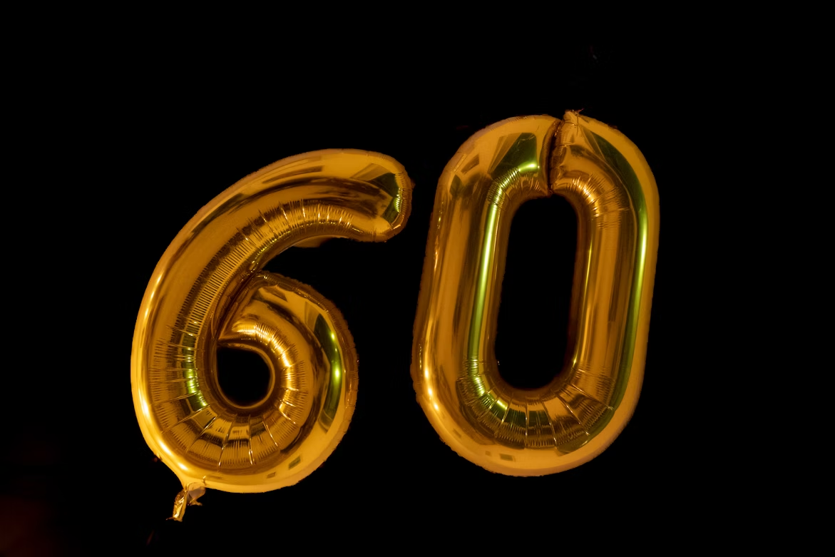Gold “60” balloons on a black background, illustrating a round-number milestone.