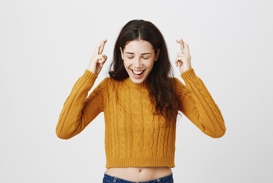 Smiling woman in mustard sweater crossing her fingers for luck