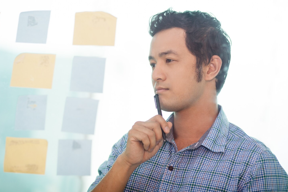 Man thinking in front of a glass wall with sticky notes, improving memory recall