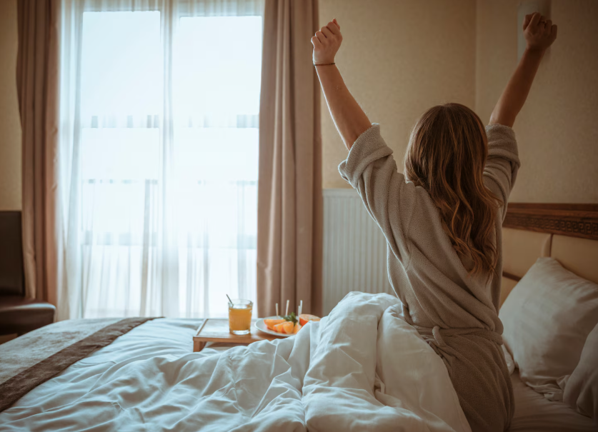 Morning stretch in a cozy bedroom, using sunlight to train her brain to like mornings.